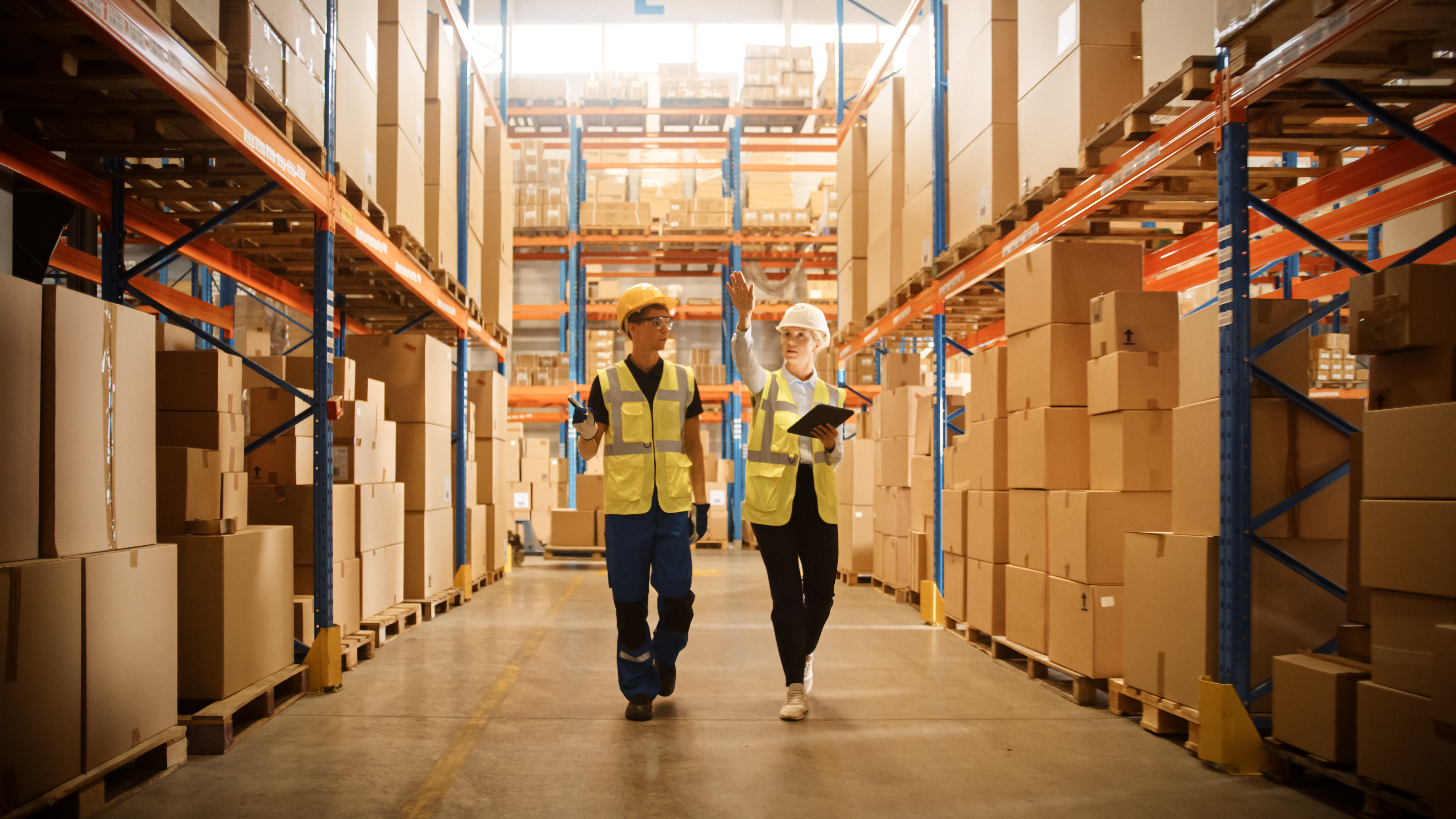 Mandlig medarbejder og kvindelig supervisor bruger en digital tablet til at gennemgå lagerlayout og optimere warehouse space i et detail-lager.